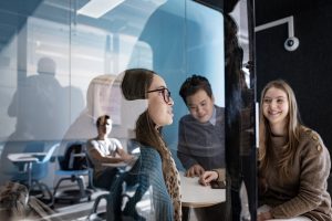 Haaga-Helia promo picture. Two young women and two men in Haaga-Helias LAB looking at each others.