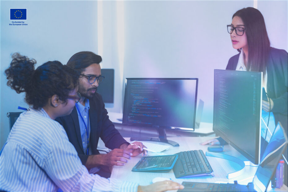 Diverse team of AI developers collaborating in a modern office. Indian male leading a discussion with Asian and Hispanic female colleagues on a machine learning project.