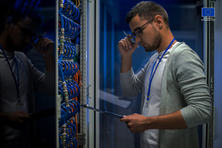 Side view portrait of young man standing by server cabinet while working with supercomputer in data center and holding clipboard