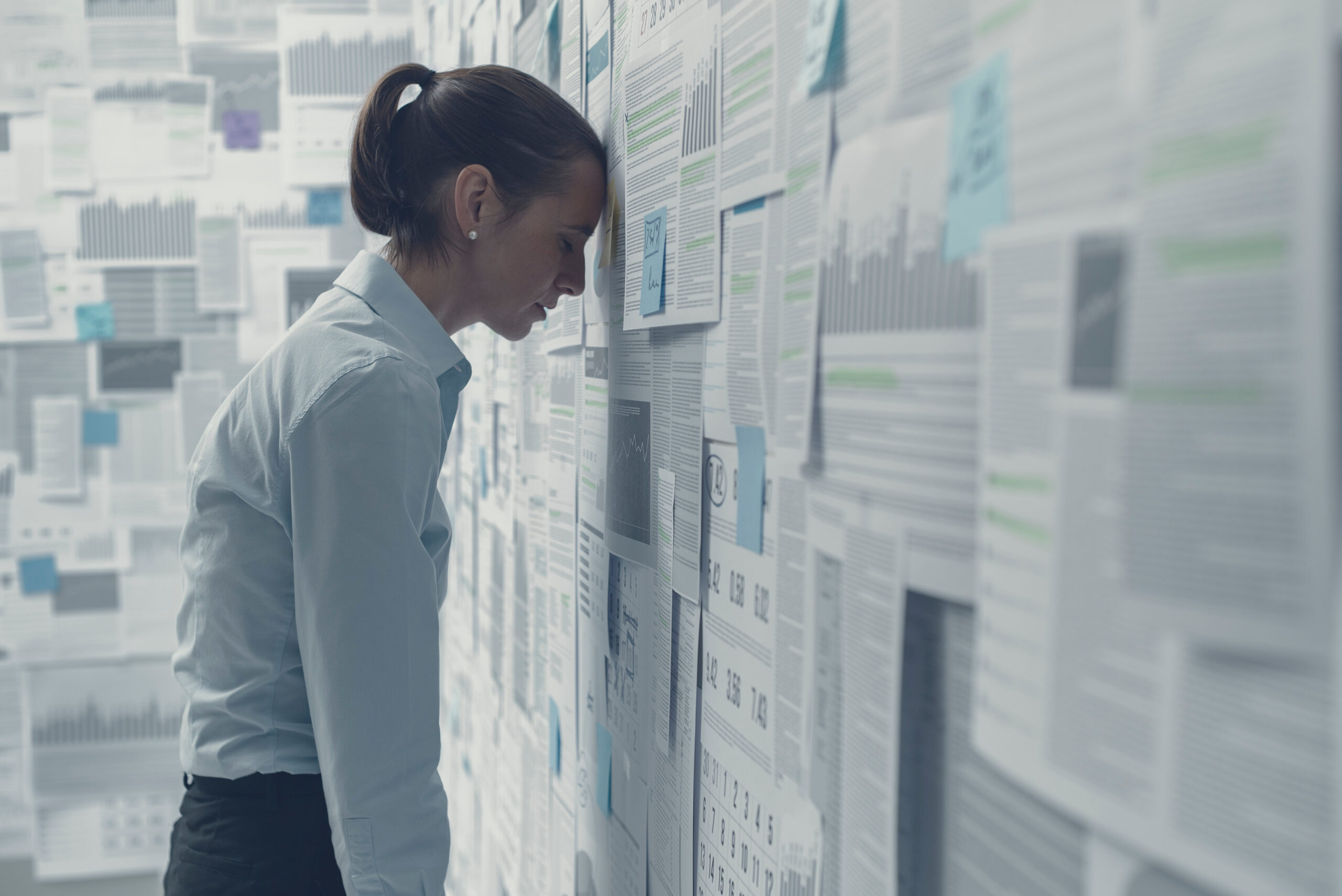 Exhausted depressed businesswoman leaning on a wall covered with financial charts and feeling hopeless, business failure concept