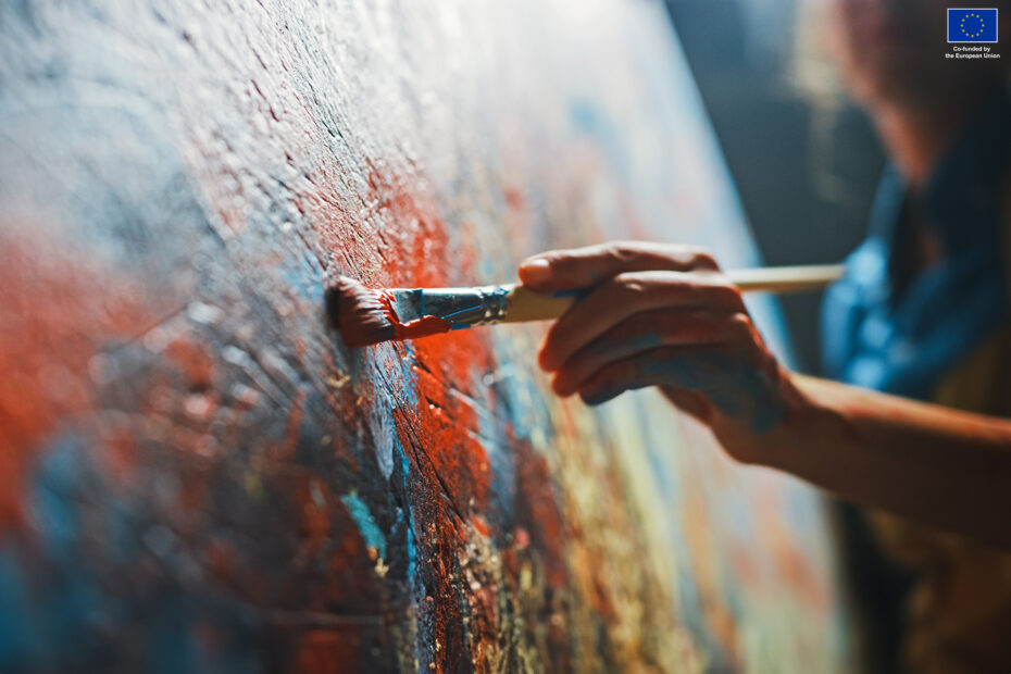 Close up of a creative artist's hands painting vibrant strokes on a canvas in artistic process in workshop